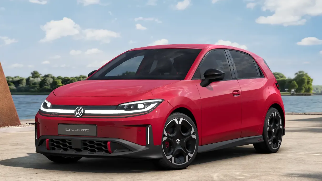 Roter VW ID. Polo GTI steht auf einer betonierten Fläche am Wasser unter blauem Himmel mit weißen Wolken.  Das Auto wirkt sportlich mit schwarzen Akzenten, großen schwarzen Felgen und LED-Frontscheinwerfern.