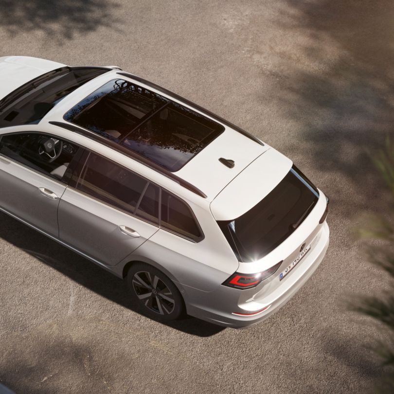 Das Bild zeigt einen Golf Variant, der auf einem gepflasterten Parkplatz steht. Der Wagen hat ein großes, dunkles Panoramadach. Die Perspektive ist von oben aufgenommen.