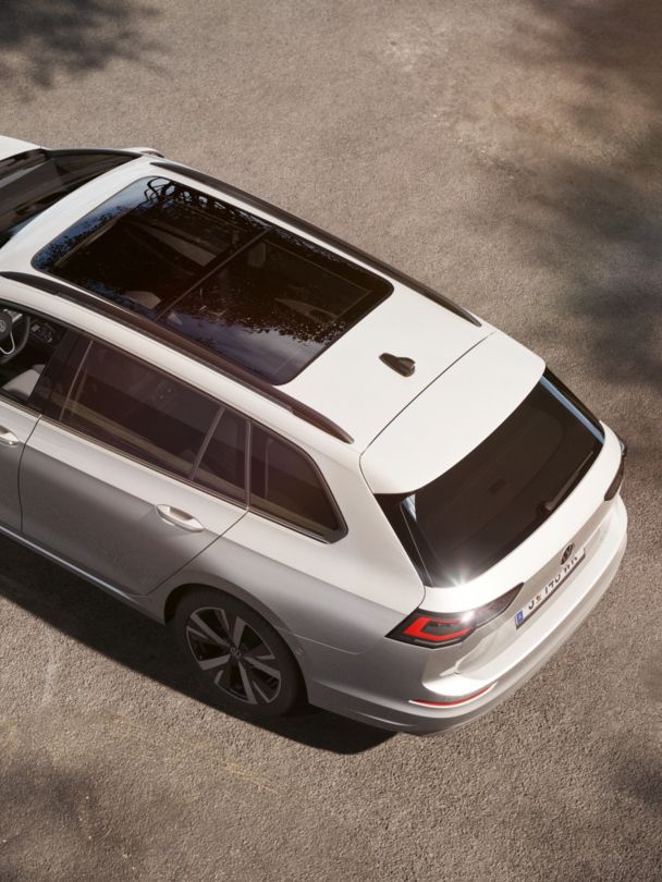 Das Bild zeigt einen Golf Variant, der auf einem gepflasterten Parkplatz steht. Der Wagen hat ein großes, dunkles Panoramadach. Die Perspektive ist von oben aufgenommen.