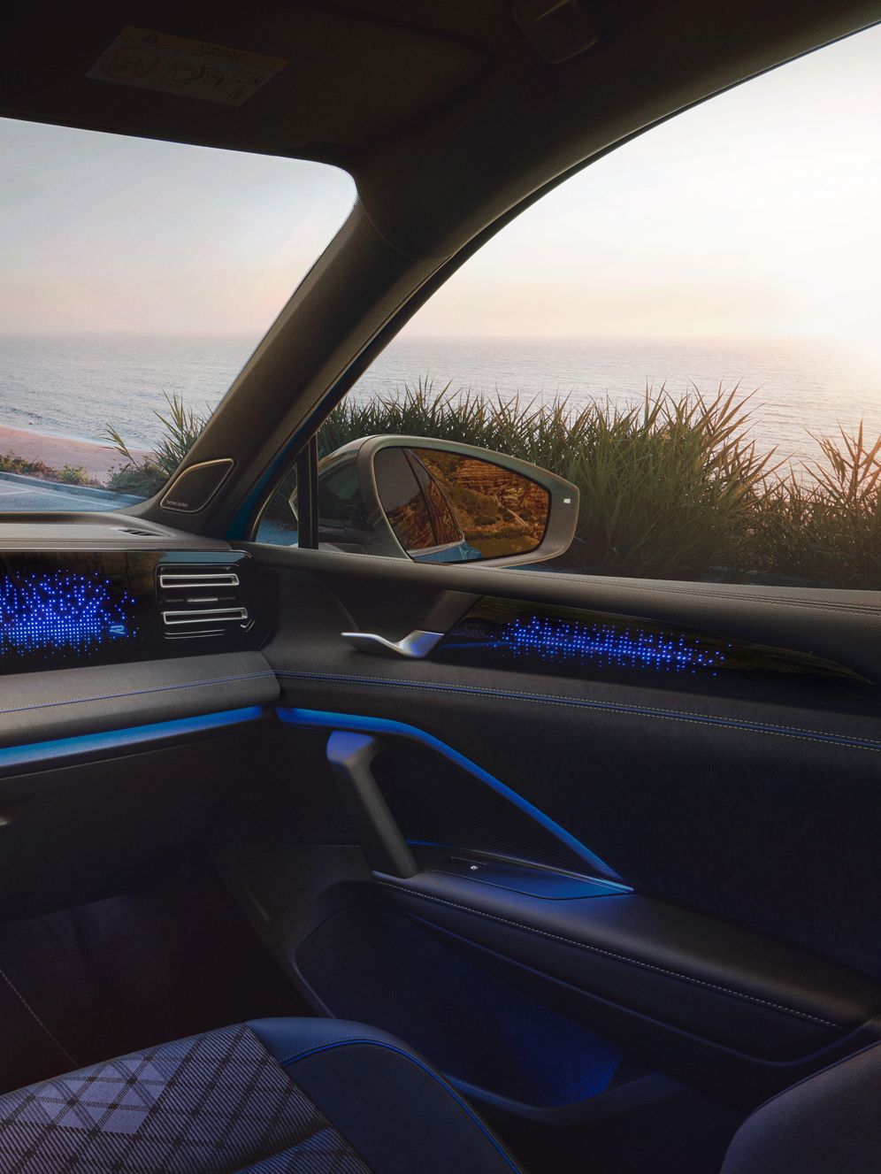 VW Tiguan mit blauer Ambientebeleuchtung. Durch die Frontscheibe ist ein Küstenlandschaft und ein auf das Meer schauendes Paar sichtbar.