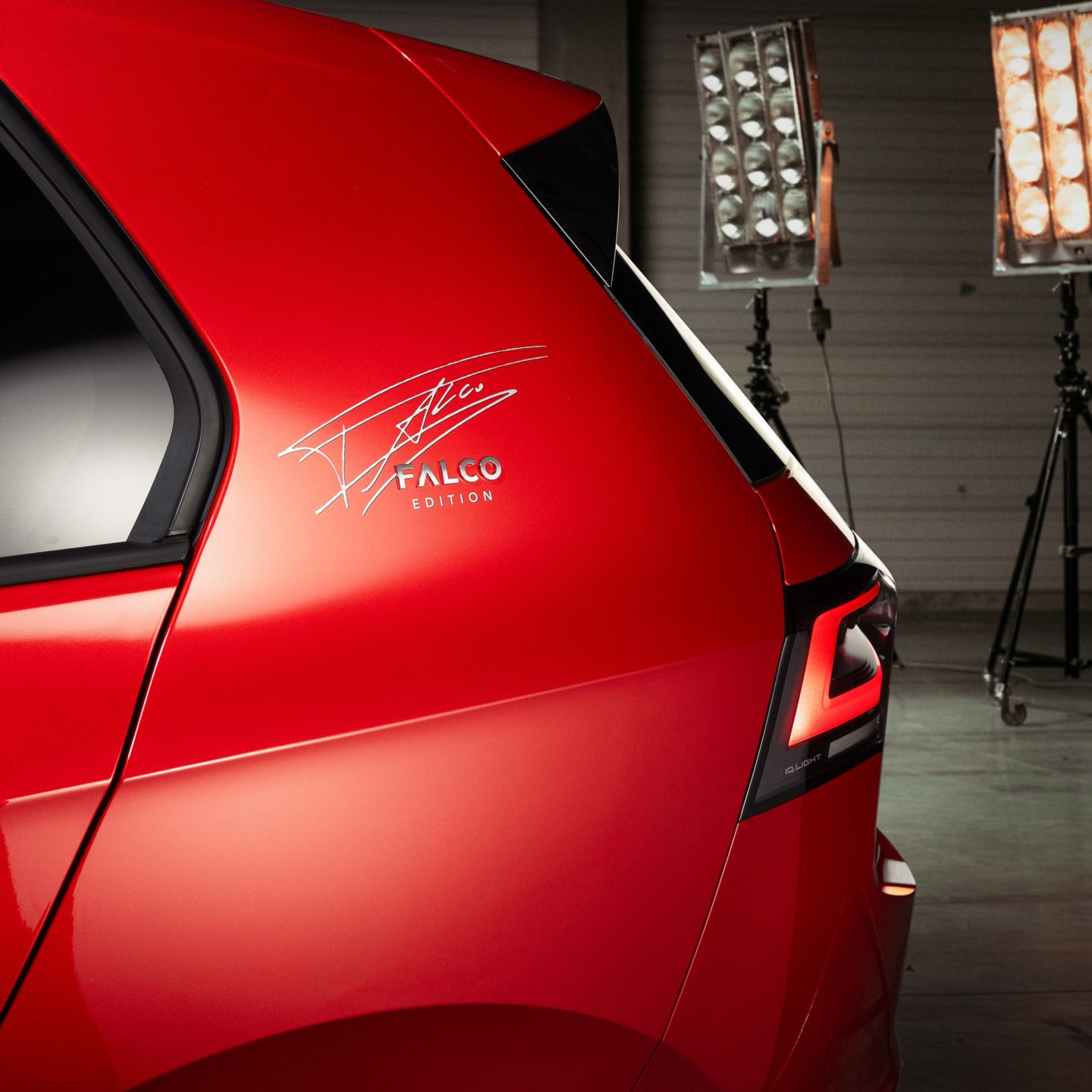 Detailaufnahme des Hecks eines roten VW Golf Falco Edition. Auf der C-Säule ist die Unterschrift von Falco zu sehen. Im Hintergrund stehen Studio Lichter