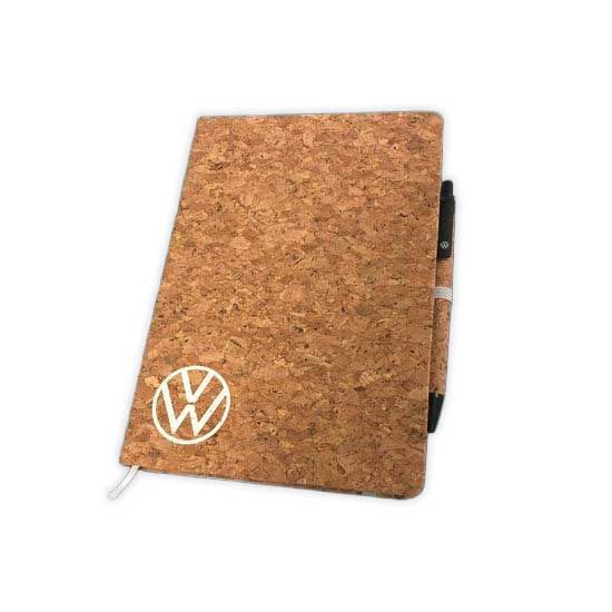 Ein Notizbuch mit Korkumschlag und dem Volkswagen-Logo auf der Vorderseite. Rechts neben dem Notizbuch steckt ein Stift.