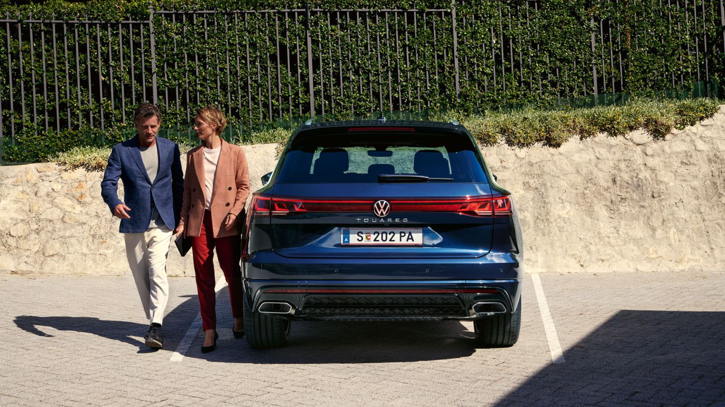 Ein Mann und eine Frau gehen am Heck des VW Touareg R-Line vorbei.