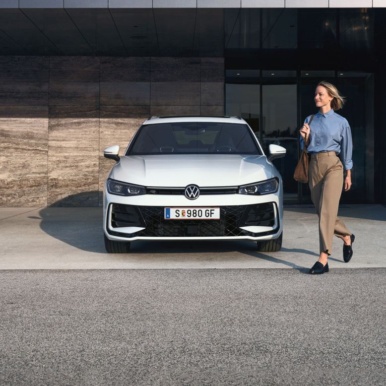 VW Passat eHybrid parkt vor Bürogebäude, eine Frau mit Tasche geht daran vorbei.