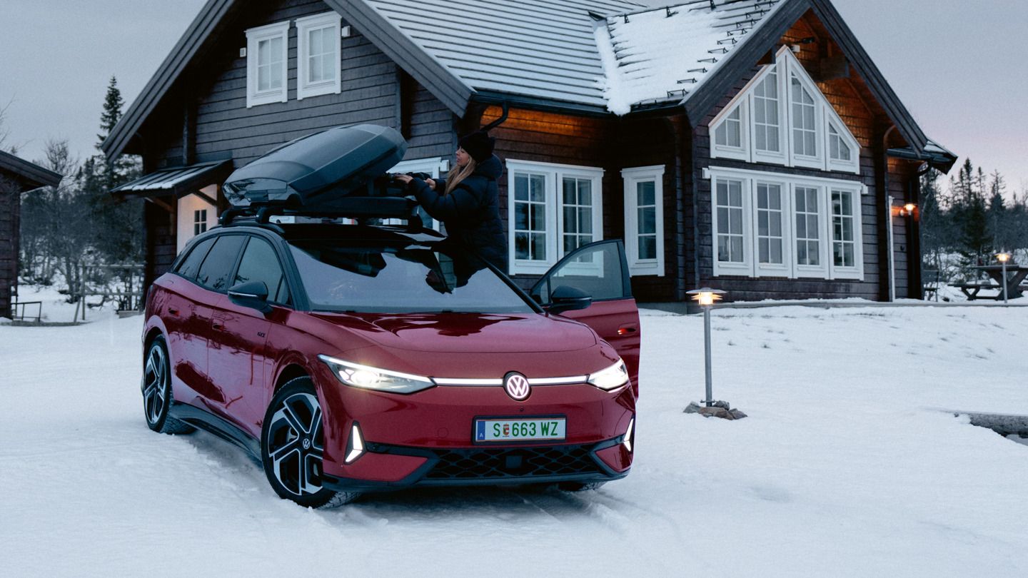 Ein roter ID.7 Tourer GTX mit Dachbox steht im Schnee vor einem Wohnhaus. 