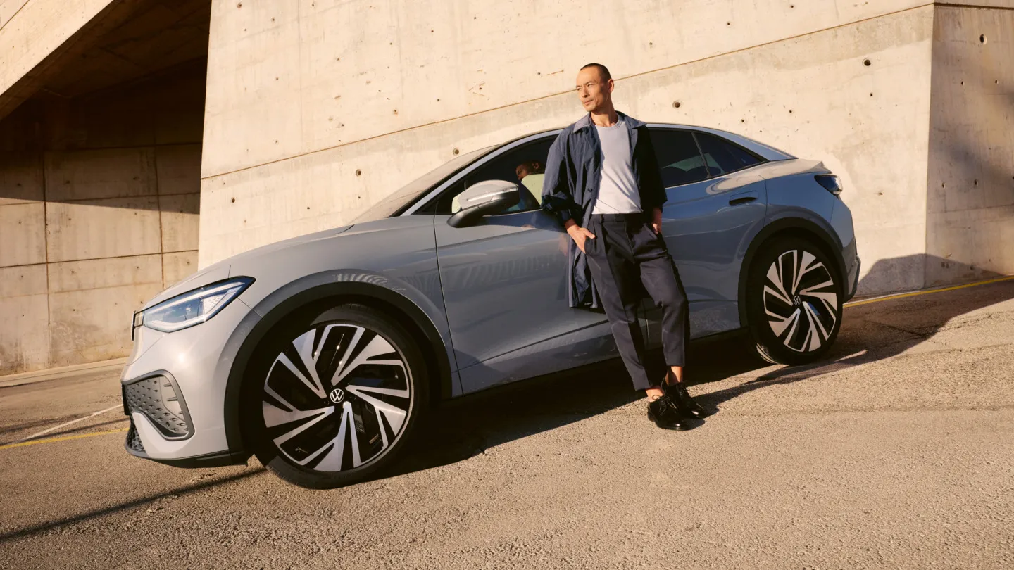 Ein grauer VW ID.5 parkt vor einem modernen Gebäude, ein Mann lehnt an der Fahrertür.