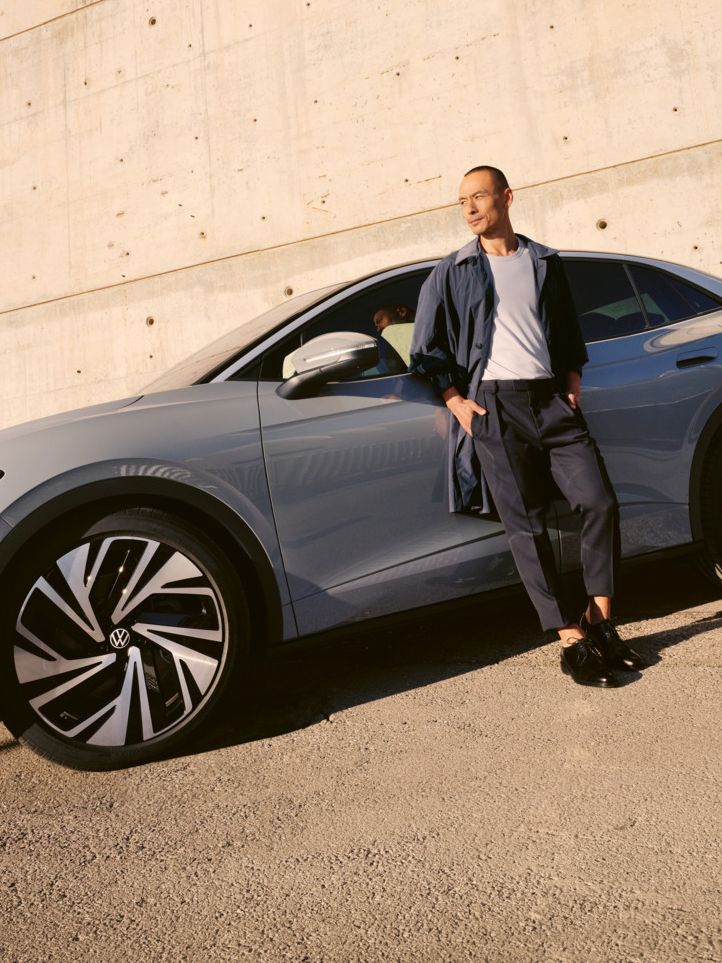 Ein grauer VW ID.5 parkt vor einem modernen Gebäude, ein Mann lehnt an der Fahrertür.