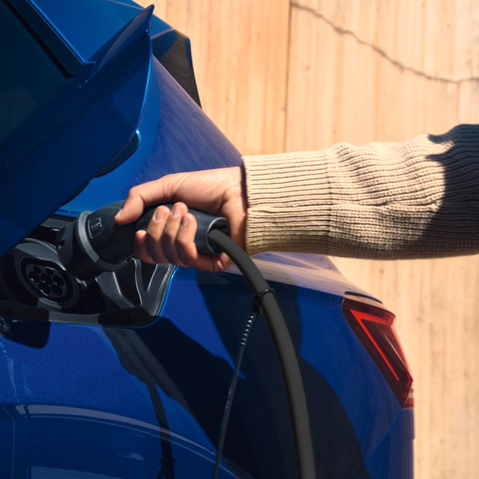 Eine Person steckt den Ladestecker in die Ladebüchse eines blauen VW Touareg.
