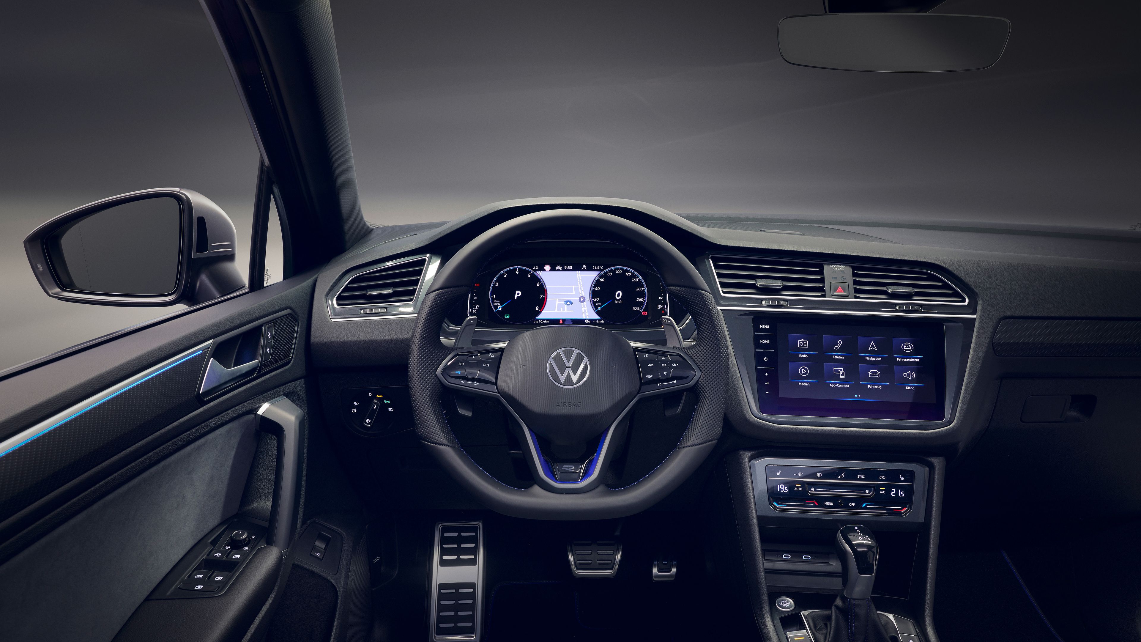 Das Bild zeigt das Interieur eines modernen VW-Fahrzeugs. Es umfasst ein digitales Armaturenbrett, einen großen Touchscreen in der Mittelkonsole und sportliche Sitze. Der Innenraum ist in Schwarz und Blau gehalten.