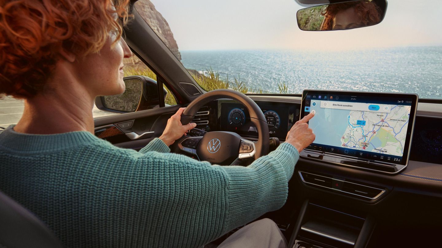  Eine Frau sitzt im VW Tiguan und bedienet das Infotainmentsystem mit Navigationsfunktion.