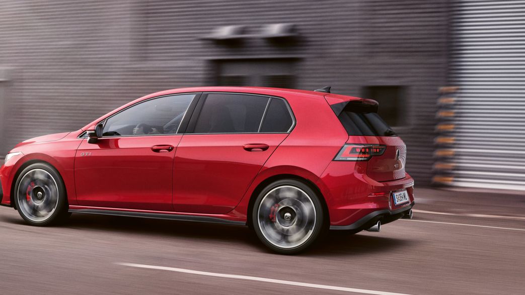 Ein roter VW Golf GTI fährt vor einer Lagerhalle entlang.