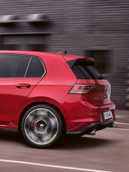 Ein roter VW Golf GTI fährt vor einer Lagerhalle entlang.