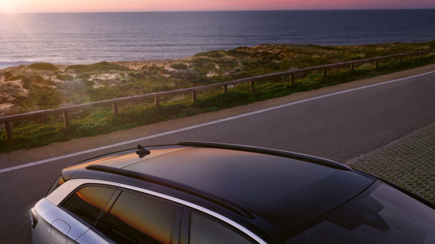 Blick auf das Panoramadach eines blauen VW ID.7 Tourer, welcher vor einer Küste parkt.