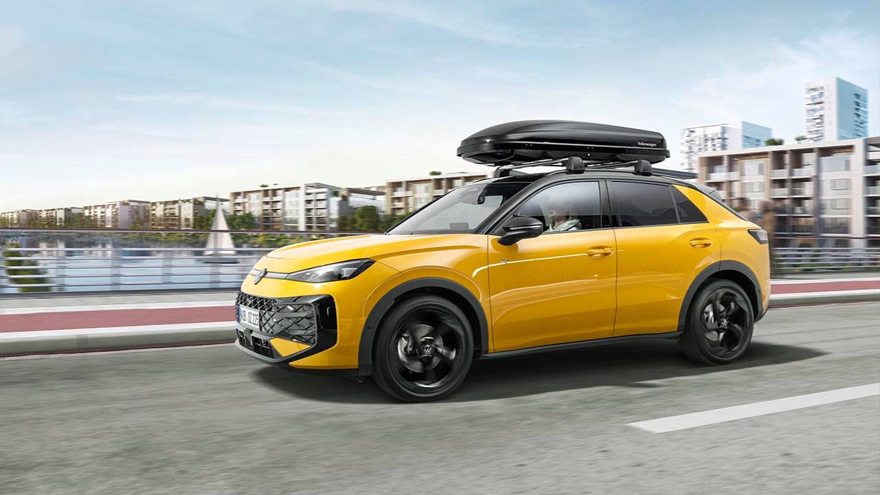 Ein gelber T-Roc mit Dachbox in Fahrt über eine Brücke.