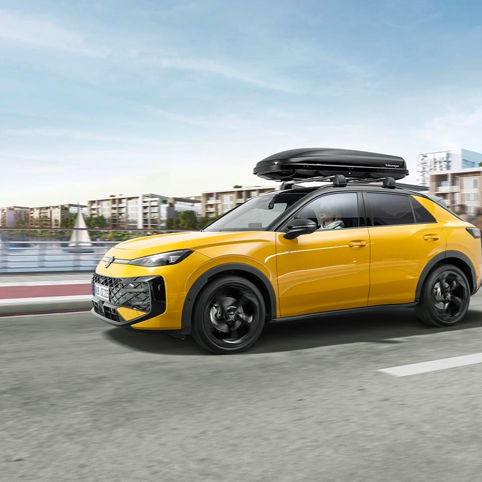 Ein gelber T-Roc mit Dachbox in Fahrt über eine Brücke.