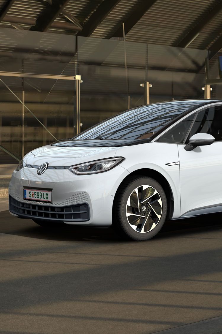 Ein weißer Volkswagen ID.3 steht in einer modernen, teilweise verglasten Tiefgarage. Das Auto ist von der Seite und leicht von vorne zu sehen. Im Hintergrund sind Maschendrahtzäune und Betonwände zu erkennen.