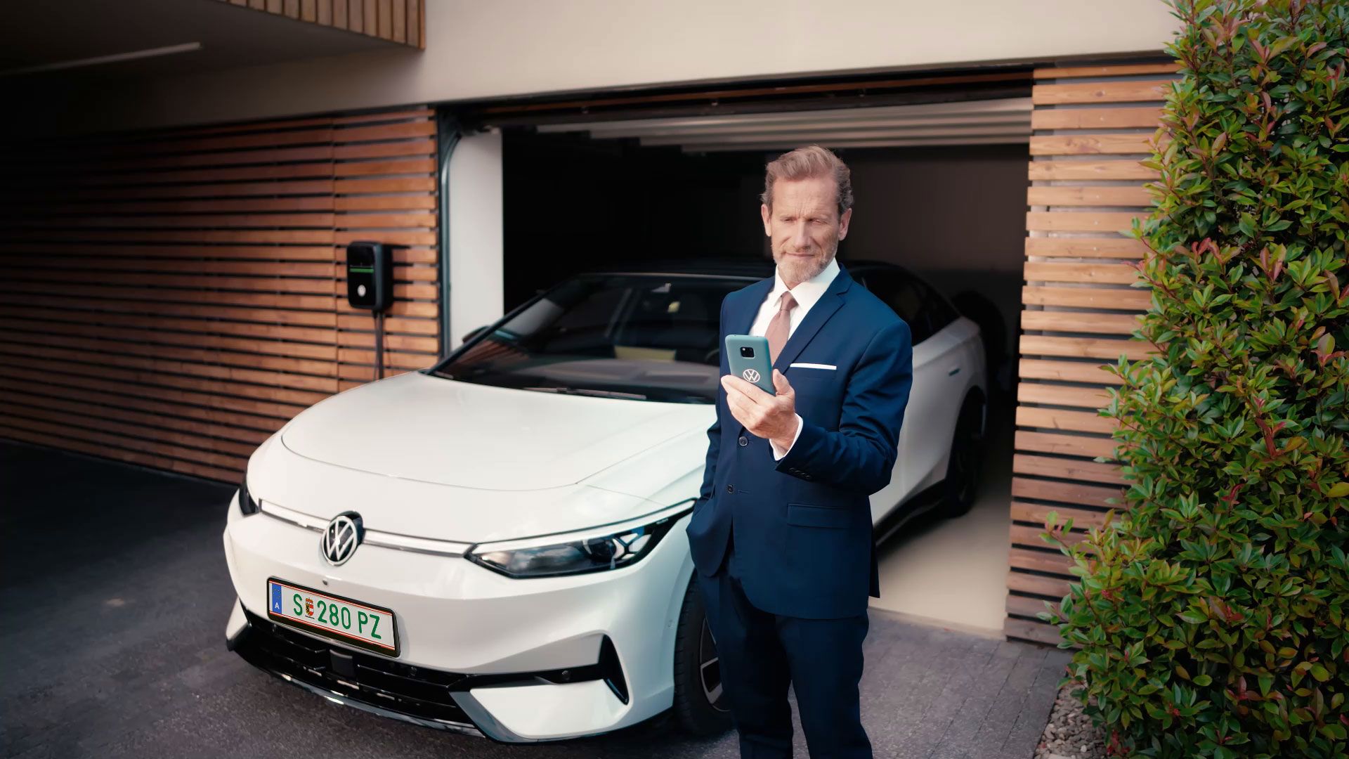 Geschäftsmann schaut auf sein Handy vor seinem in der Garage geparkten ID.7