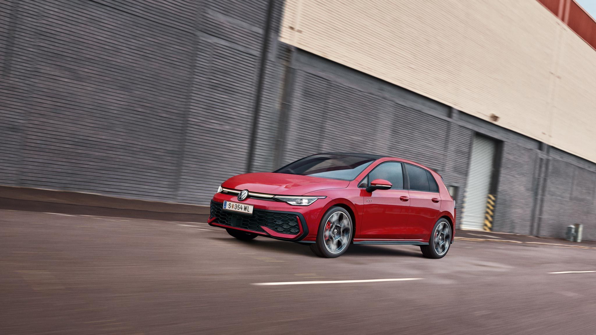 Ein roter VW Golf GTI fährt vor einer Lagerhalle entlang.