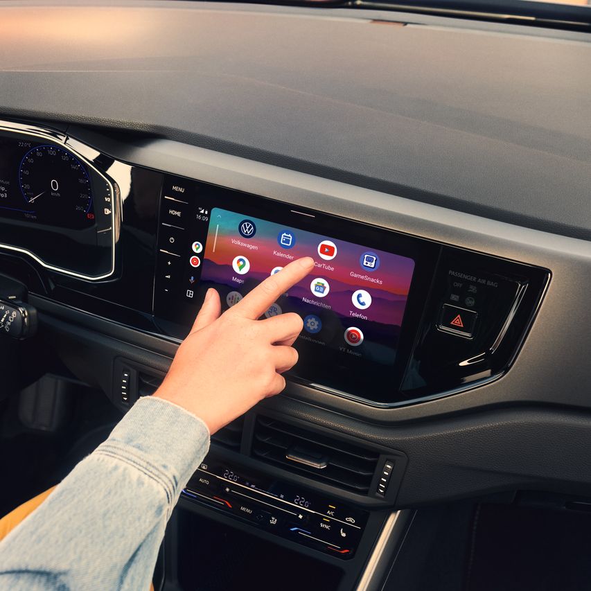 Eine Hand wählt ein App-Symbol im Menü des Infotainment-System eines VW Polo aus.