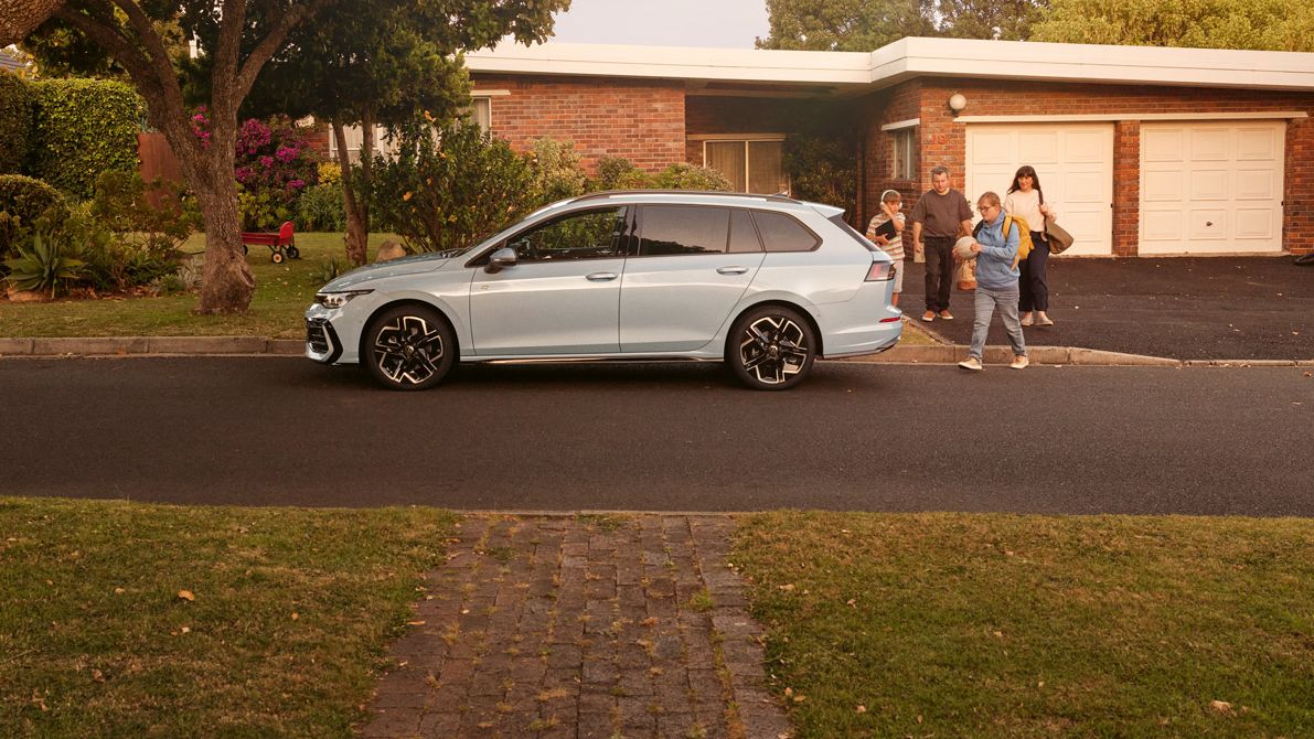Ein weißer VW Golf Variant parkt vor einem Bungalow in einer Wohnstraße mit Bäumen. 