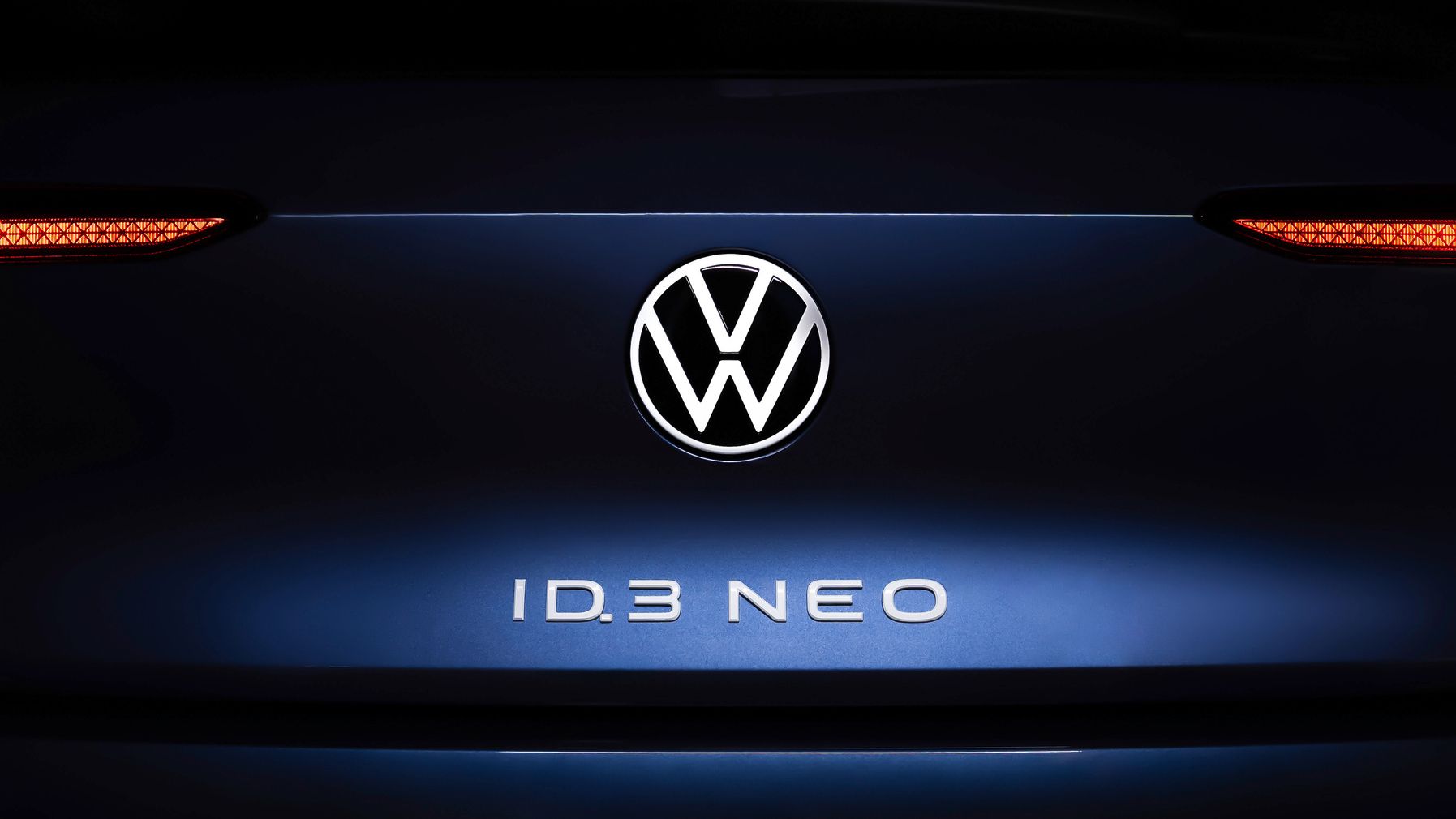 Nahaufnahme des Hecks eines Volkswagen ID.3 NEO. Im Zentrum ist das Volkswagen-Logo beleuchtet, darunter steht der Schriftzug "ID.3 NEO". Die Rücklichter sind auf beiden Seiten des Logos sichtbar.