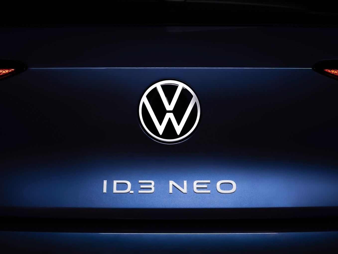 Nahaufnahme des Hecks eines Volkswagen ID.3 NEO. Im Zentrum ist das Volkswagen-Logo beleuchtet, darunter steht der Schriftzug "ID.3 NEO". Die Rücklichter sind auf beiden Seiten des Logos sichtbar.
