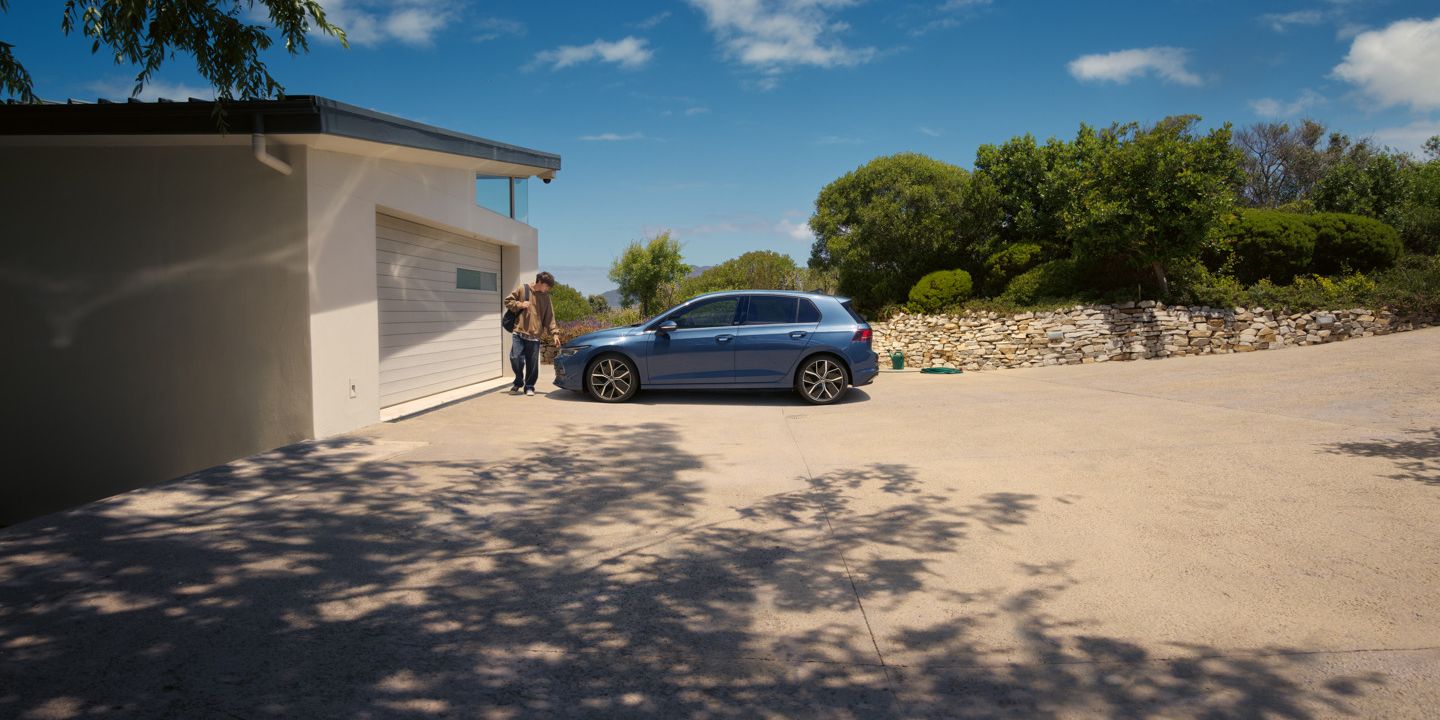 Ein junger Mann geht an einem blauen VW Golf vorbei