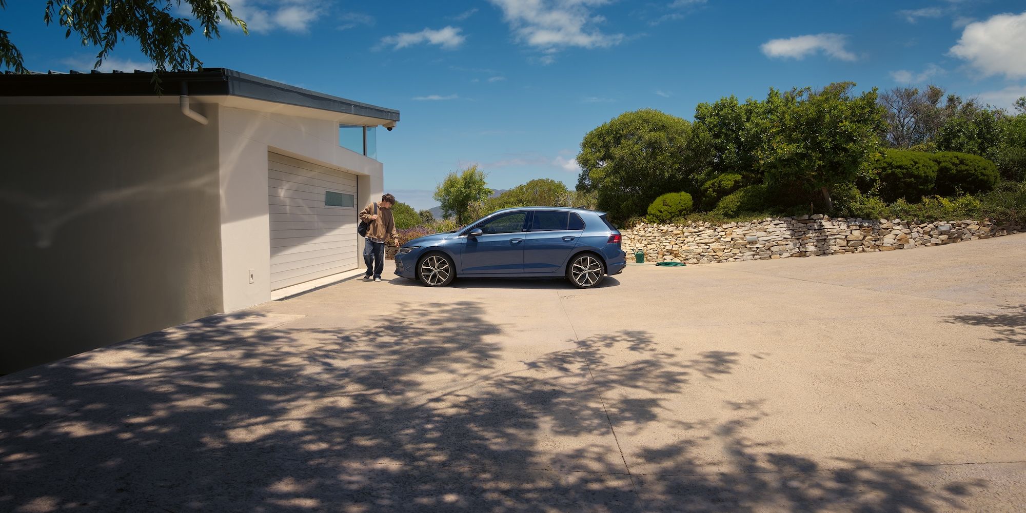 Ein junger Mann geht an einem blauen VW Golf vorbei