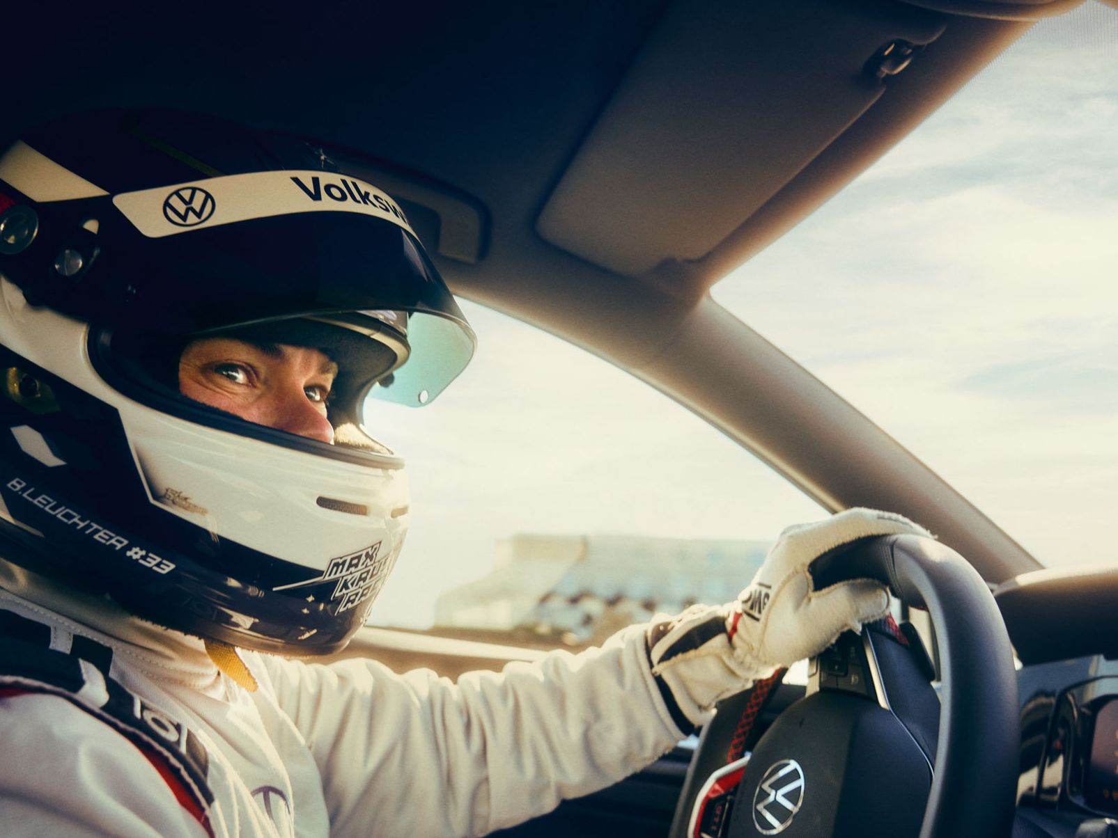 Golf GTI Fahrer aus Sicht des Beifahrers mit Helm und Hand am Lenkrad.