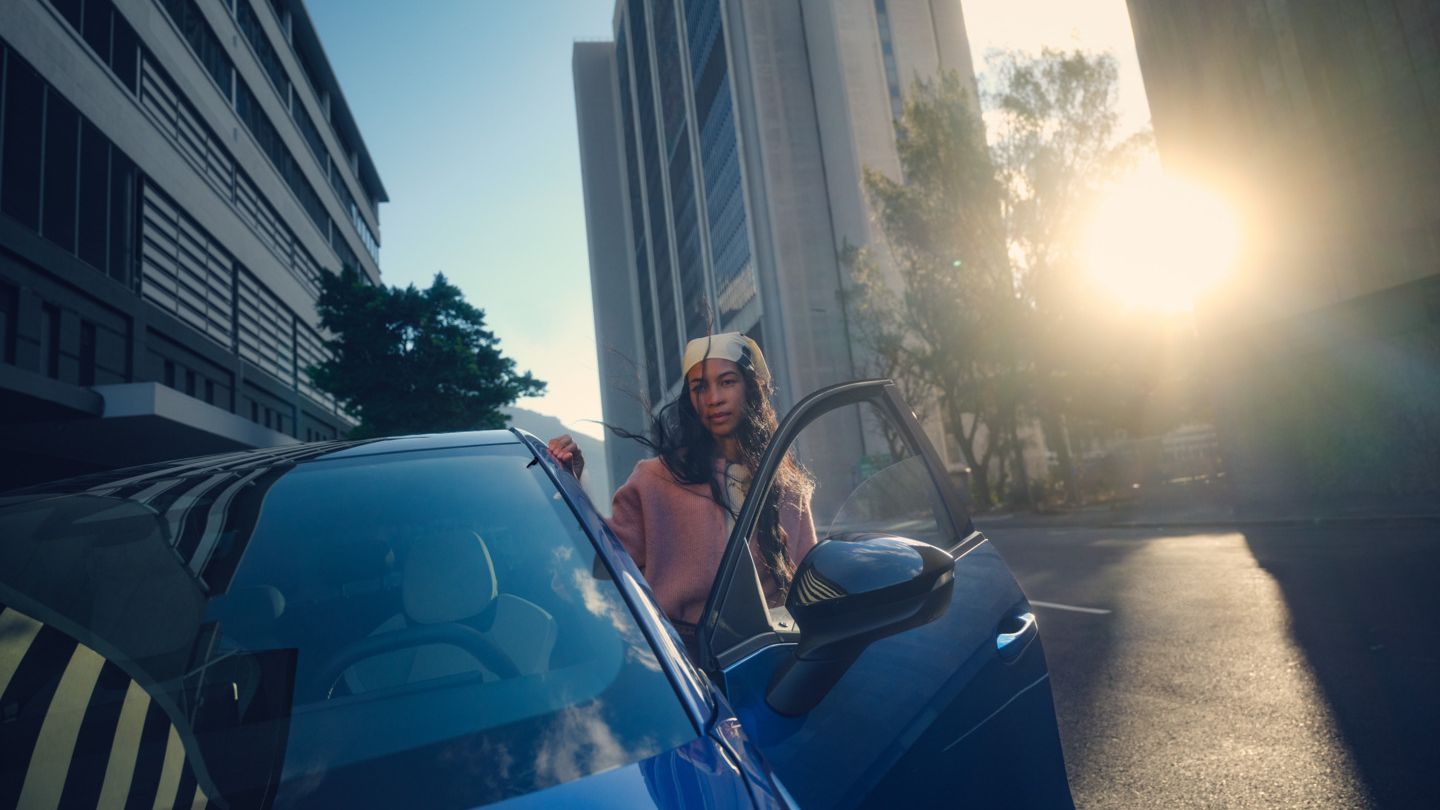 Ein blauer VW ID. Polo Style parkt in einer Stadt im Sonnenuntergang, eine Frau steigt auf der Fahrerseite aus.