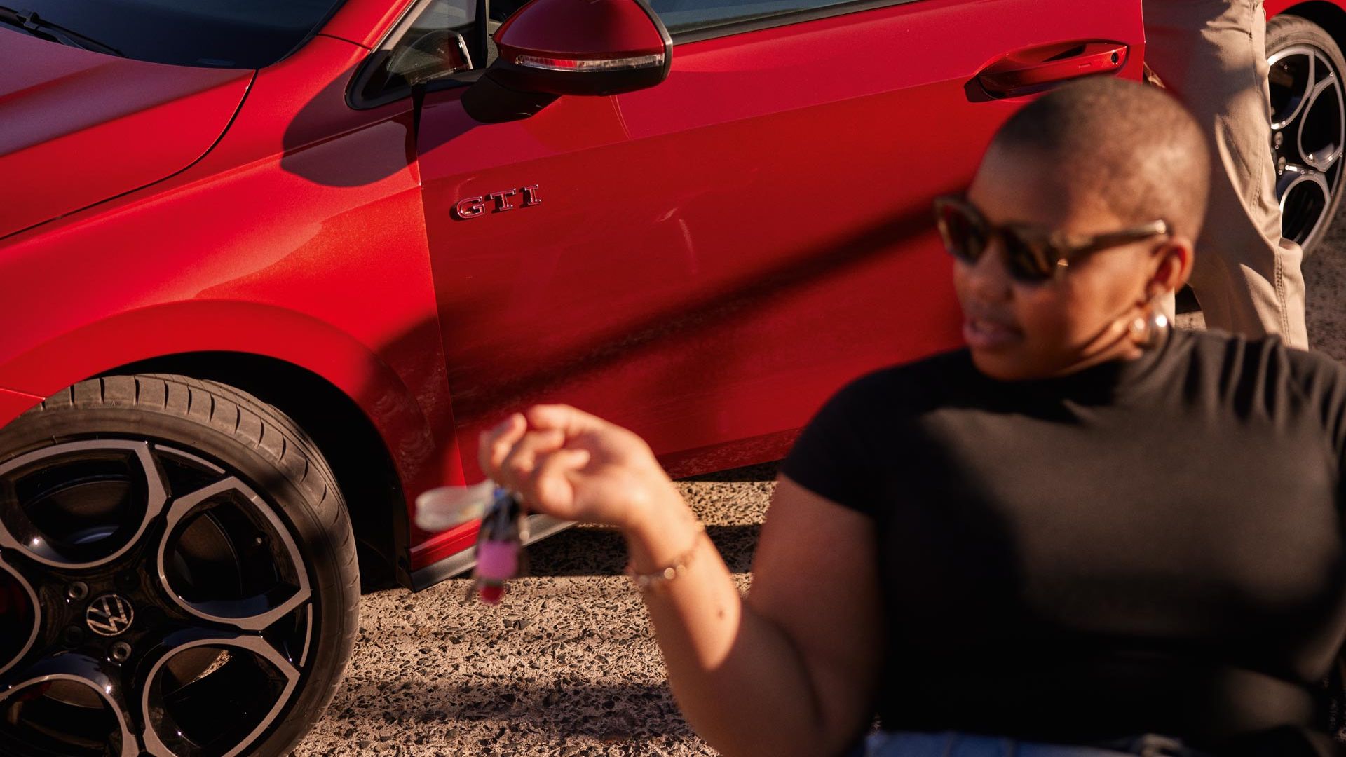 Eine Frau hält einen Schlüsselbund in der Hand und entfernt sich  von einem roten VW Golf GTI.