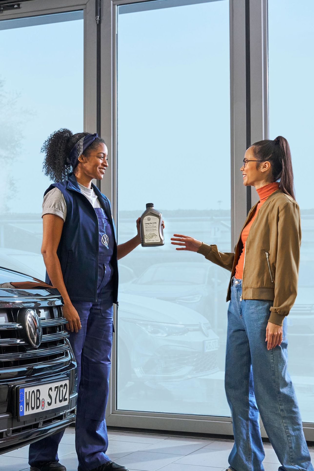 Eine Volkswagen Service Technikerin überreicht einer Kundin eine Ölflasche.