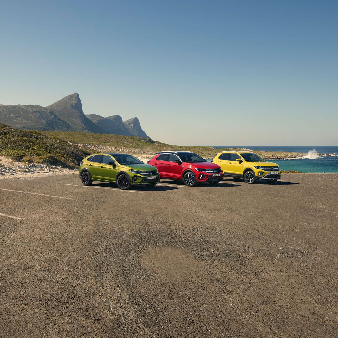 Taigo, T-Roc, T-Cross stehen geparkt auf einem Parkgelände, im Hintergrund sieht man das Meer.