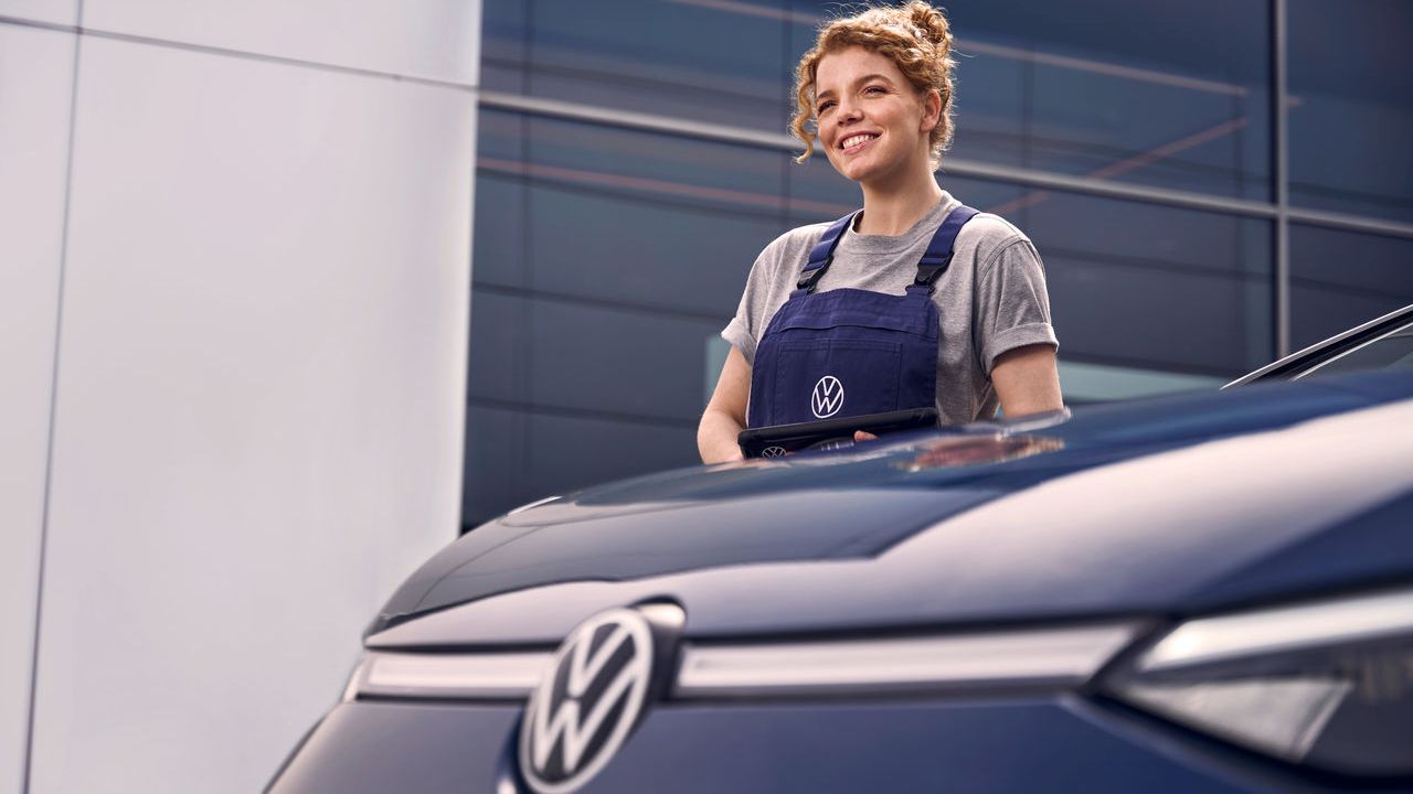 Eine Volkswagen Technikerin vor einer Volkswagen Werkstatt.