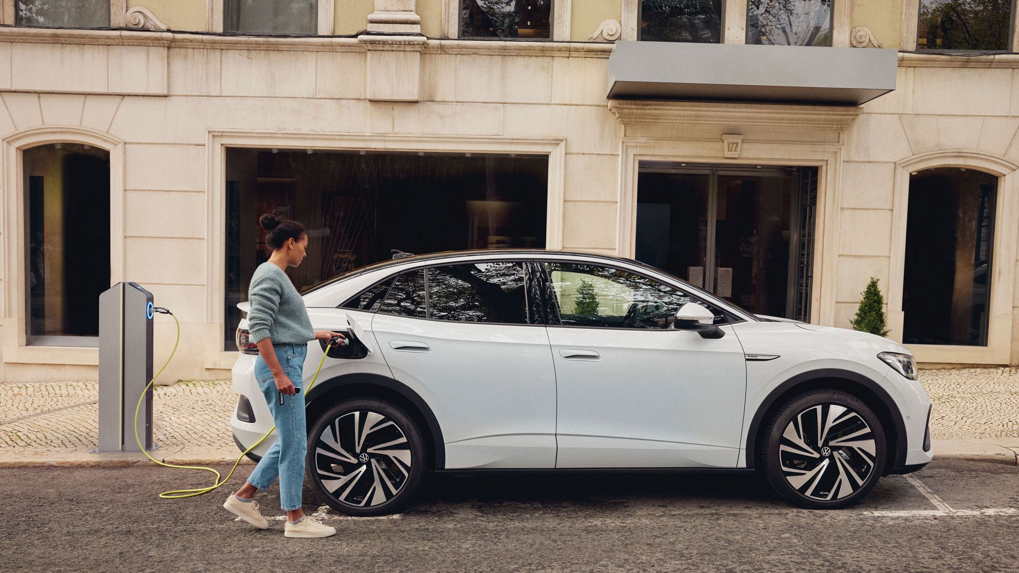 Eine Frau hat ihren Volkswagen ID. an einer Ladesäule geparkt und steckt den Ladestecker in das Fahrzeug.