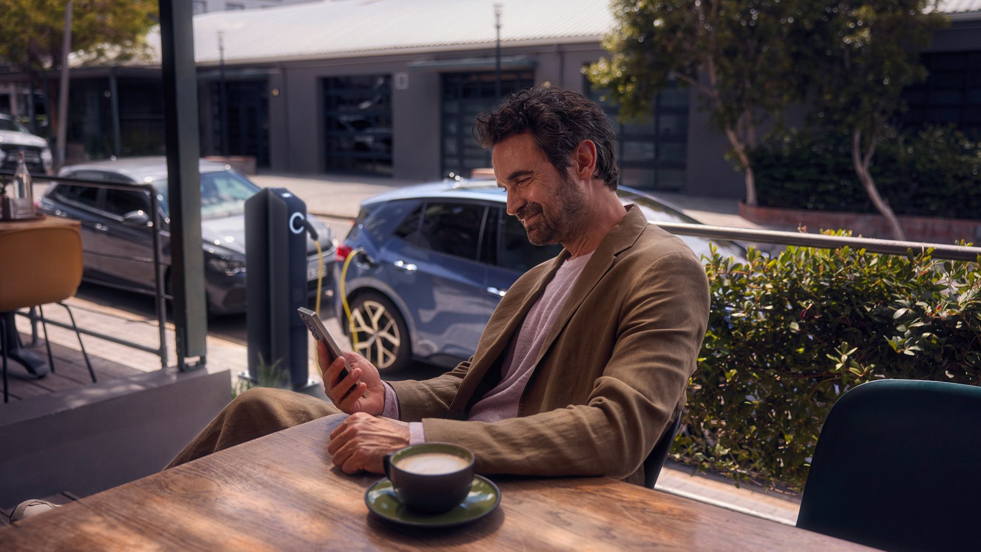 Ein Mann sitzt im Café und checkt per Smartphone den Ladestatus seines VW ID.3 Neo