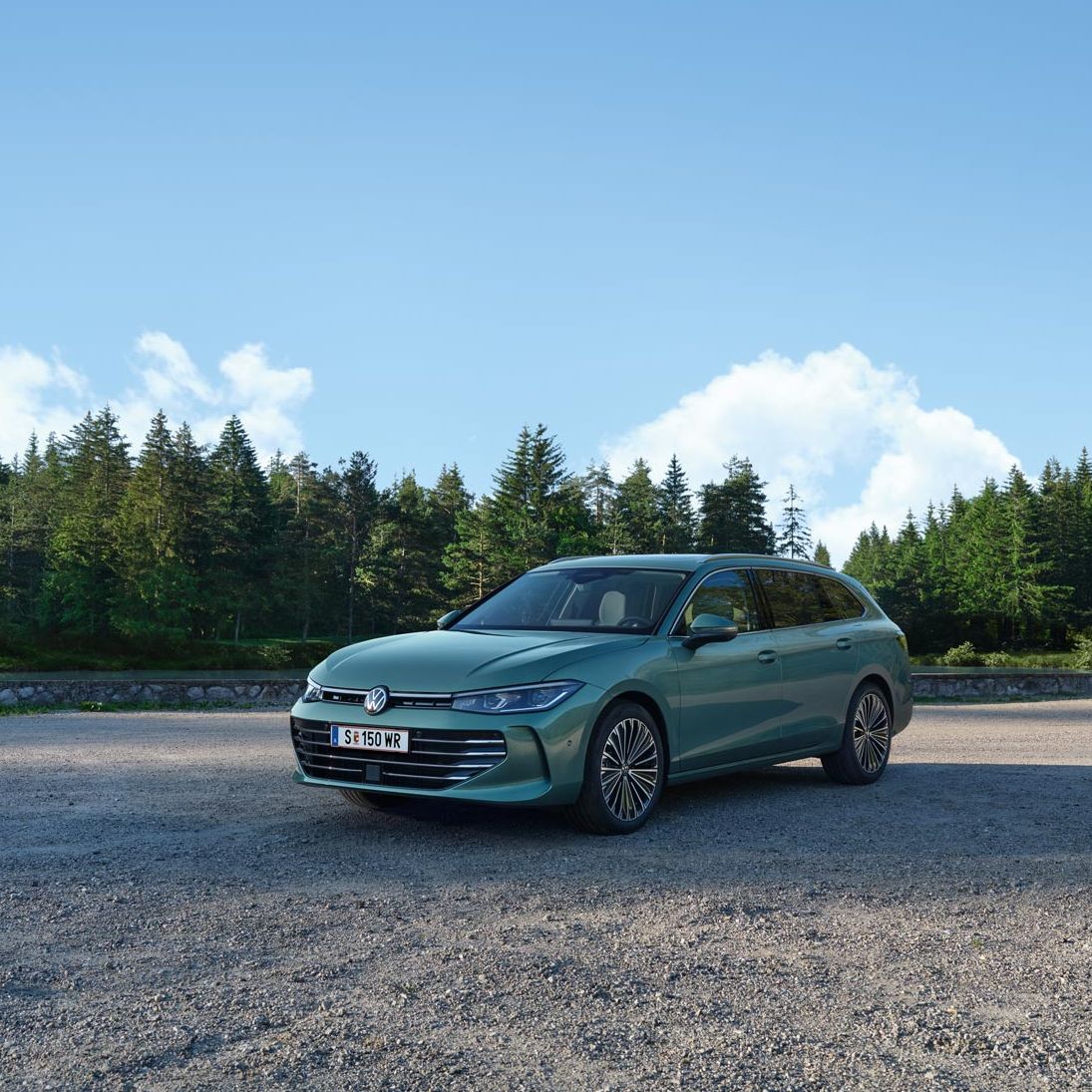 VW Passat in blaugrün steht auf einer Kiesfläche, im Hintergrund ein Tannenwald.