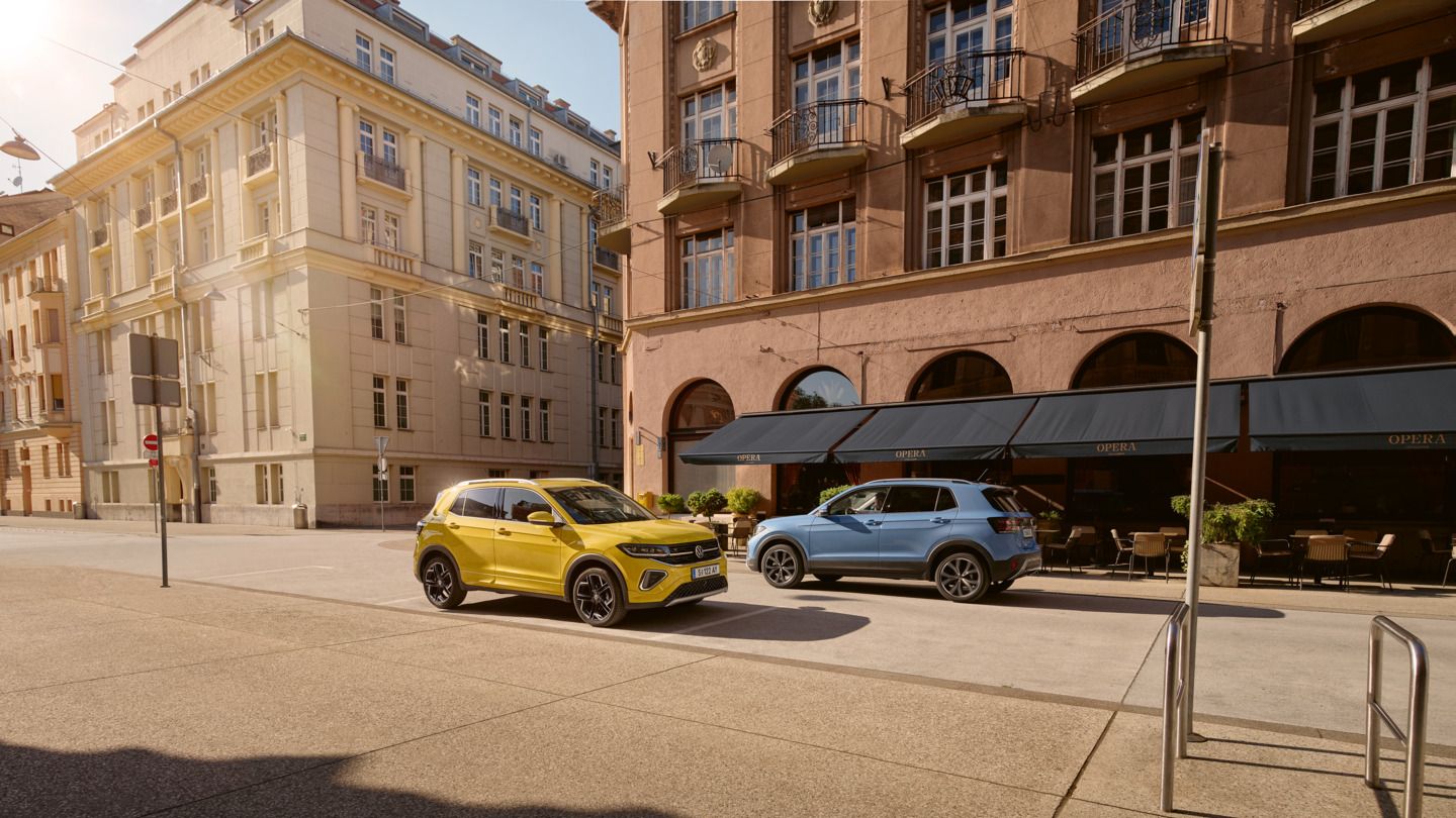 Ein gelber VW T-Cross parkt am Straßenrand in einer Stadt. Ein blauer T-Cross fährt diesem entgegen.