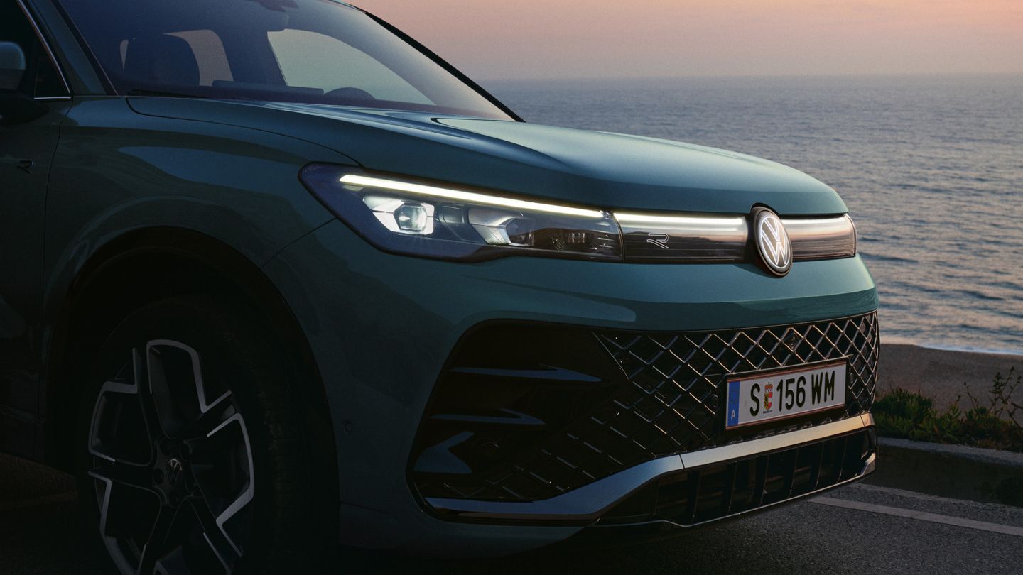 Front-Lichtsignatur eines blauen VW Tiguan am Meer beim Sonnenuntergang.