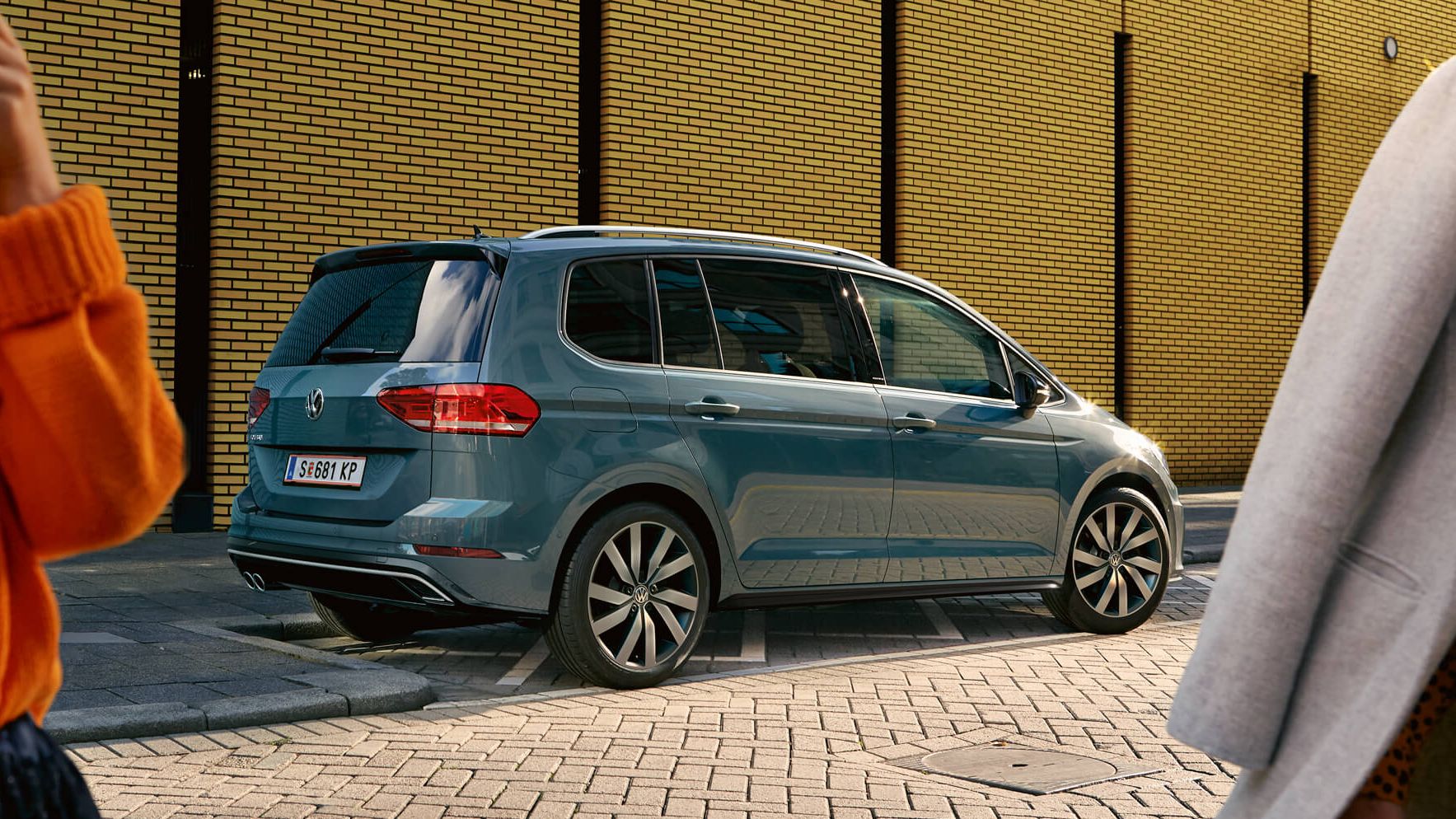Zu sehen ist eine Frau die gerade die Türe eines VW Fahrzeuges schließt. Im Hintergrund sieht man einen Mann der beim Kofferraum steht.