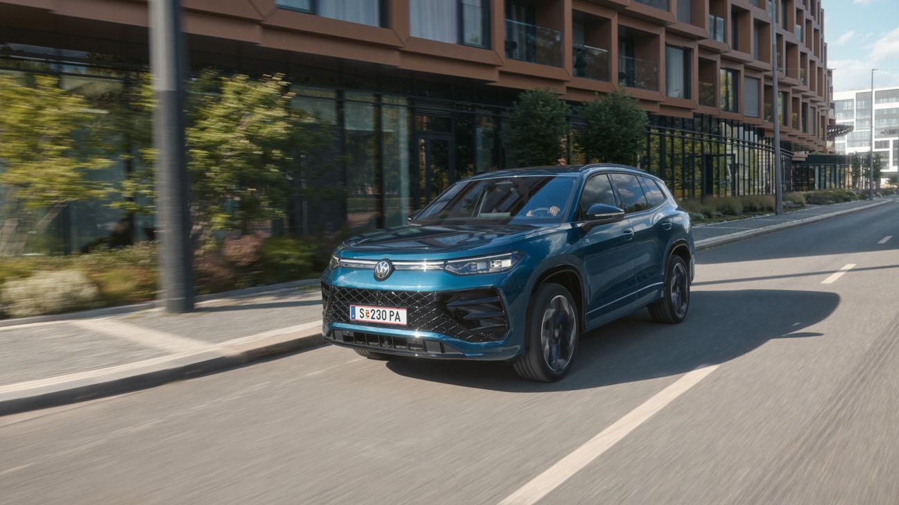 Ein VW Tayron R-Line Plug-In-Hybrid fährt vor modernen Gebäuden in einer urbanen Umgebung.