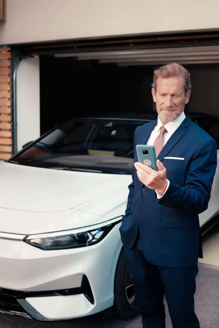 Geschäftsmann schaut auf sein Handy vor seinem in der Garage geparkten ID.7