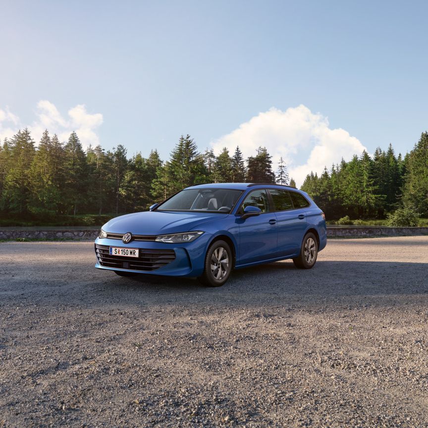 VW Passat in blau steht auf einer Kiesfläche, im Hintergrund ein Tannenwald.