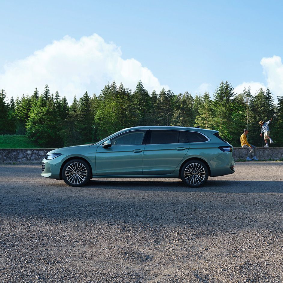 Seitenansicht eines grünen VW Passat Elegance vor einem Wald, im Hintergrund sieht man einen Mann und einen Jungen.