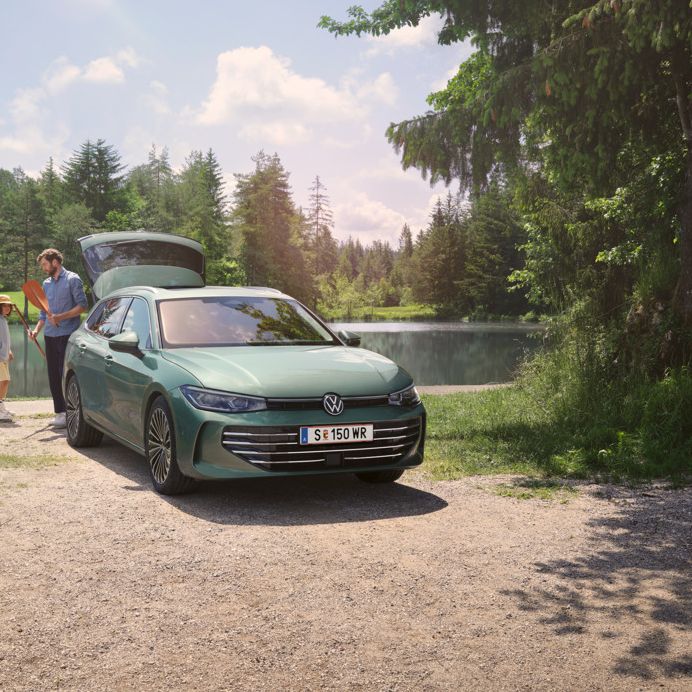 Der neue VW Passat Elegance in Maripositgrün Metallic parkt an einem Badesee mit geöffnetem Kofferraum. Ein Mann verteilt Freitzeitspielzeug an zwei Kinder.