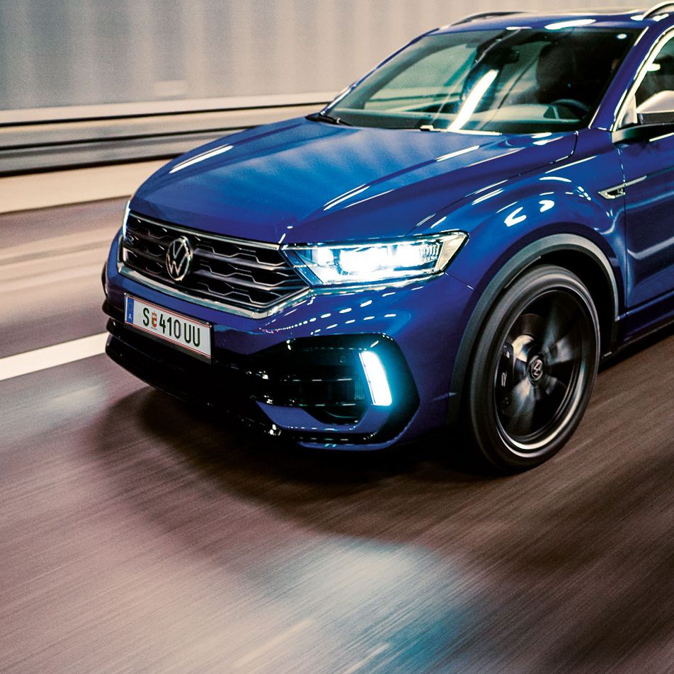 Ein blauer VW T-Roc fährt schnell durch einen beleuchteten Tunnel. Das Auto sieht modern und sportlich aus. Die Straßenmarkierungen sind deutlich auf dem Boden sichtbar.
