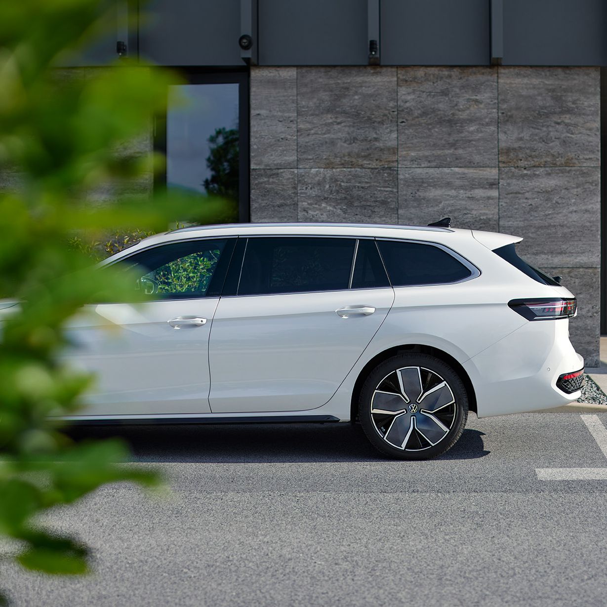 Ein weißer VW Passat steht geparkt vor einem Haus, die Front ist leicht durch einen Busch im Vordergrund verdeckt