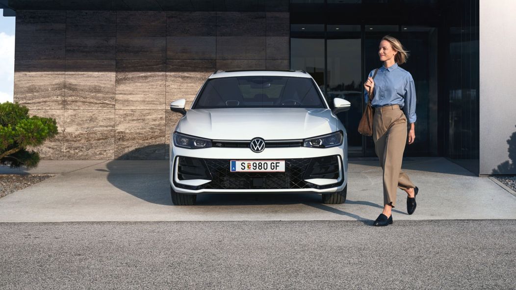 VW Passat eHybrid parkt vor Bürogebäude, eine Frau mit Tasche geht daran vorbei.