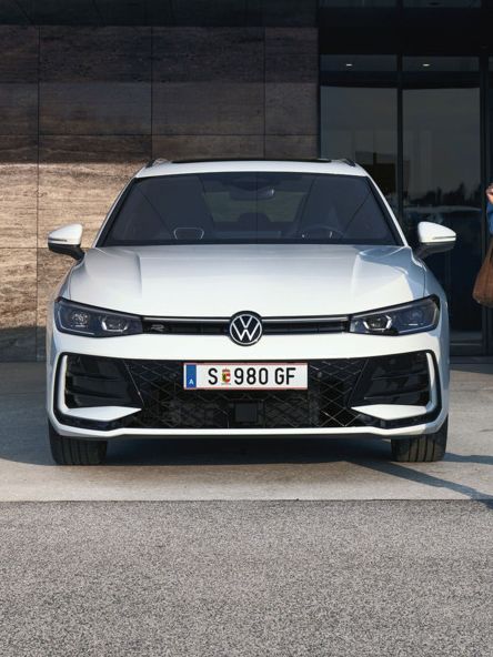 VW Passat eHybrid parkt vor Bürogebäude, eine Frau mit Tasche geht daran vorbei.