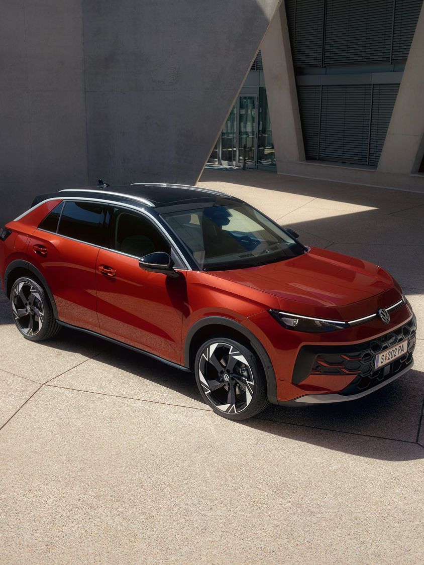 Ein roter VW T-Roc Style steht vor einem modernen Gebäude im Sonnenlicht